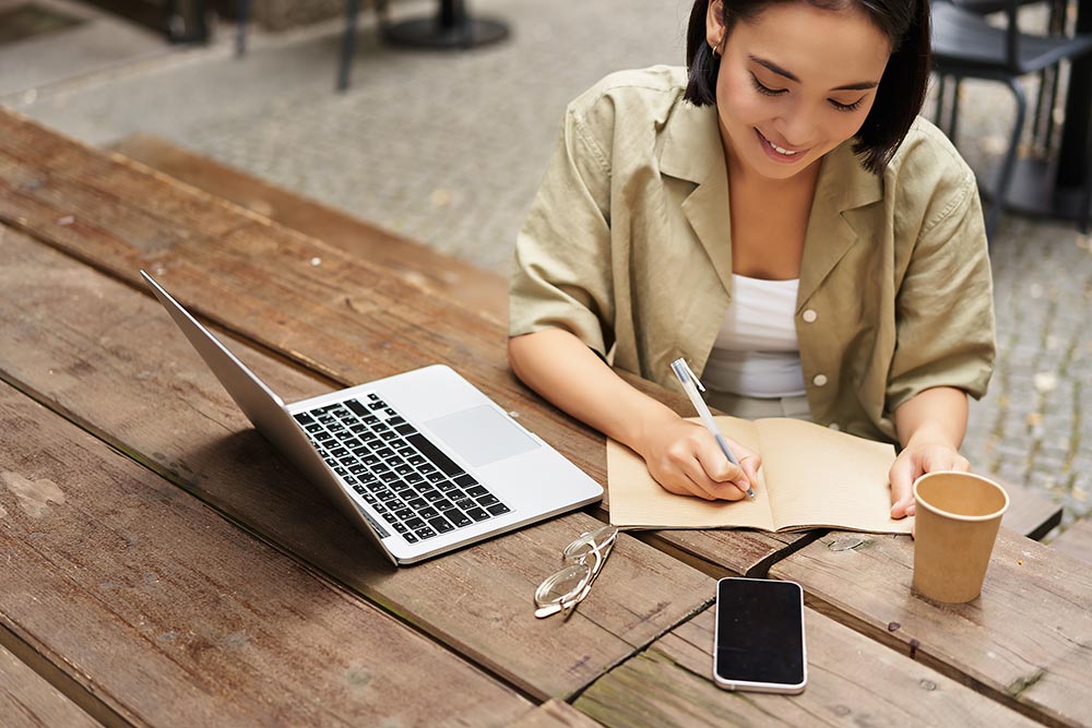 portrait-young-woman-studying-online-sitting-with-laptop-writing-down-making-notes-looking2